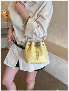 Detail of yellow quilted leather bucket bag with metal chain strap worn by a model