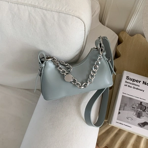 Detail of light blue crescent bag with silver chain on soft white furniture texture