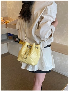Chic yellow quilted bucket bag with silver chain strap worn by a model in a cafe