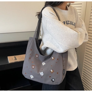 Detailed close-up of colorful cat embroidery and brand tag on a gray canvas tote bag