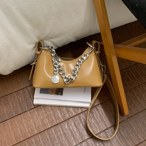 Detail of light brown leather bag with chunky silver chain and round metal tag on books