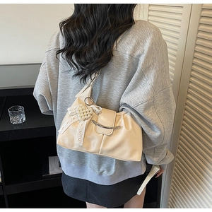 Detail of beige pleated shoulder bag featuring a pearl lace bow and metal clasp