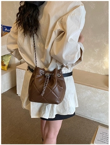 Close-up of a brown quilted bucket bag with silver metal chain drawstring and strap