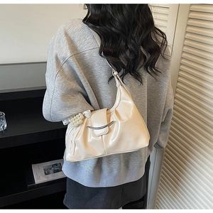 Close-up of beige moon-shaped shoulder bag featuring pearl charms and crescent buckle
