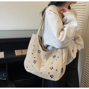Close-up of cute cat and bear embroidery on beige canvas tote bag with side brand tag