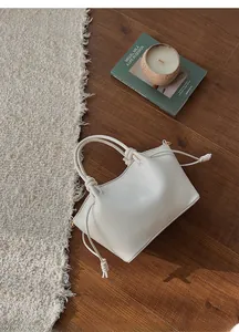Detail of cream white drawstring handbag with knot handles on a cozy home rug