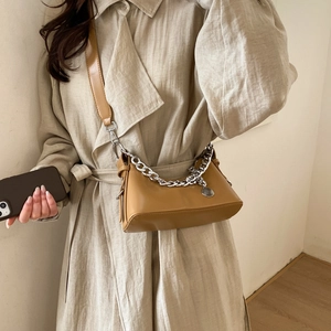 Close-up of a khaki shoulder bag featuring bold silver chain and round metal pendant