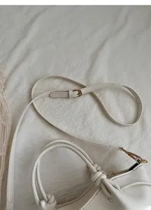Detail of adjustable slim shoulder strap and light gold buckle on cream white handbag