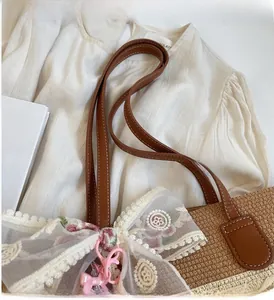 Détail du sac en paille avec anses en cuir robustes et nœud en dentelle blanche fleurie