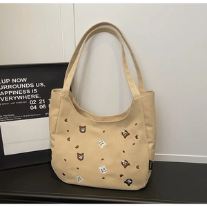 Detailed embroidery of a cartoon bear on a beige canvas tote bag with side label
