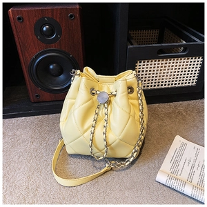 Detail of quilted bright yellow bucket bag featuring leather-woven chain and drawstring