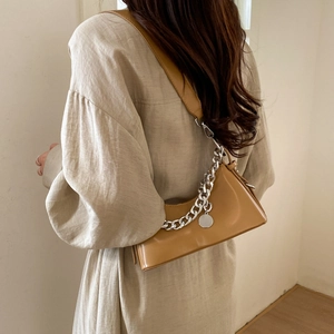 Detail of camel baguette bag featuring a bold silver chain and round metal tag