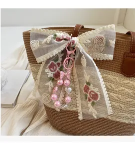 Détail d'un nœud en dentelle brodé de fleurs avec perles roses sur sac de paille
