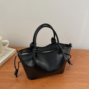 Detail of black leather handbag with braided handle knots and gold hardware on wood surface
