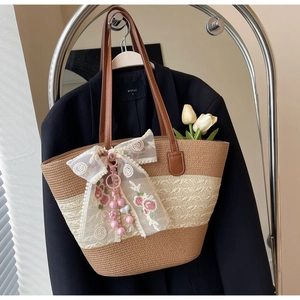 Détail d'un sac cabas en paille avec nœud en dentelle blanche et pendentif fleur perlé