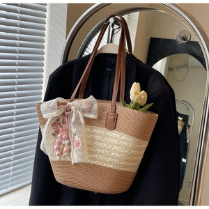 Détail d'un sac cabas en paille tissée avec nœud en dentelle et broderie de fleurs