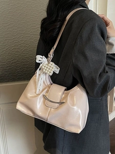 Chic beige hobo bag with pearl bow charm worn on shoulder over grey blazer