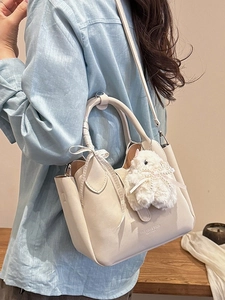Chic beige bucket bag with ribbon bow and plush rabbit charm shown on model's shoulder