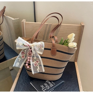 Détail du cabas en paille avec rayures noires, anses en cuir et nœud en dentelle brodé de fleurs