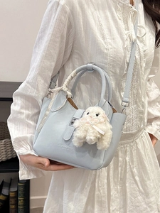 Light blue crossbody bucket bag with ribbon handle and fuzzy charm on a fashion model