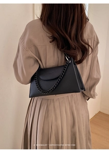 Detail of black lychee texture leather handbag with chunky chain strap on a model