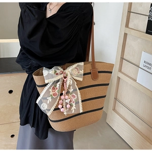 Détail du sac cabas en paille avec nœud en dentelle florale et breloque cœur en perles
