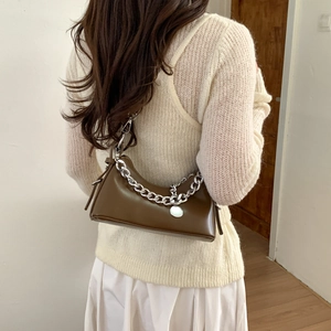 Detail view of brown leather bag with silver chain strap worn by a model