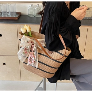 Détail du sac cabas en paille avec nœud en dentelle blanche, broderie et charm perlé