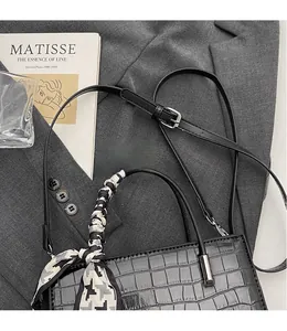 Detail of black crocodile texture handbag with geometric silk scarf on a gray suit