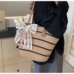 Détail du sac cabas en paille avec nœud en dentelle blanche et pendentif en perles roses