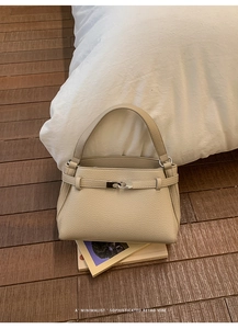 Detail of beige lychee grain leather handbag with silver turn-lock on a wooden background