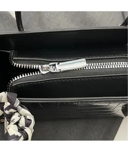 Close-up of a black handbag featuring silver metal zipper and crocodile texture detailing