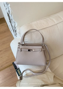 Detailed close-up of elephant grey lychee texture leather bag on a cream sofa