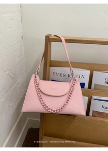 Pink lychee grain leather crossbody bag with chain detail on a magazine rack