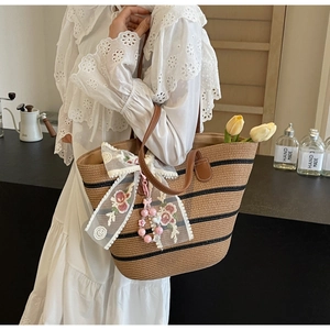 Détail du sac cabas en paille avec rayures noires, nœud en dentelle et anses cuir