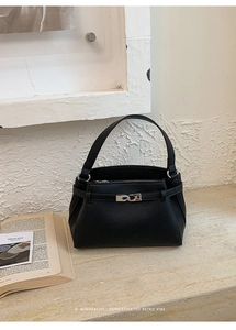 Detail of black lychee grain leather handbag with silver twist-lock on marble surface