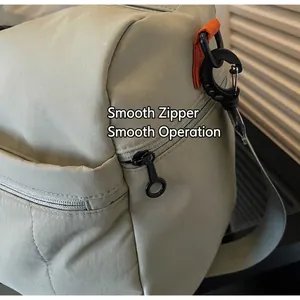 Close-up of smooth black metal zipper and reinforced orange strap on beige travel bag