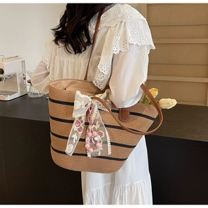 Détail d'un sac cabas en paille tressée à rayures noires avec bandoulière en cuir et nœud