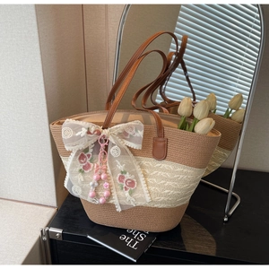 Détail du sac en paille tissée avec nœud en dentelle, broderie florale et breloque perle