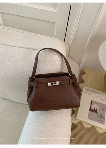 Detail of dark brown lychee grain leather handbag with silver lock on a white sofa