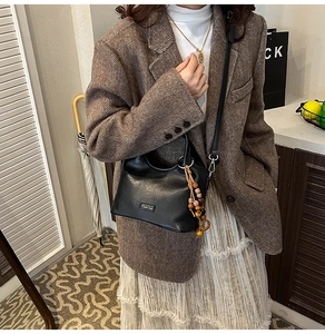 Chic black leather bucket bag with decorative beads worn with a brown blazer and white skirt