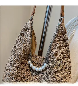 Détail du sac hobo en paille tressée avec chaîne argentée, perles et bandoulière en cuir
