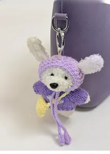 Détail d'un pendentif ours en peluche blanc avec pull violet et sac jaune sur un sac