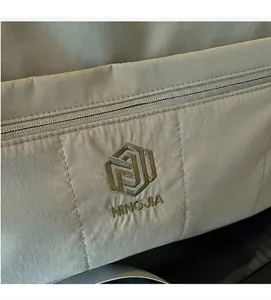 Detail showing khaki ripstop nylon texture with zipper and NINGJIA embroidery
