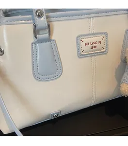 Detail of blue and beige tote bag featuring a brand label and a soft plush ball charm
