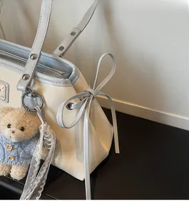 Detail of cream tote bag featuring blue trim, a decorative bow and plush bear charm