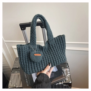 Detalle de bolso tote de punto verde oscuro con etiqueta de cuero artesanal en fondo de viaje