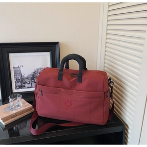Close-up of wine red travel bag featuring reinforced handles and embroidered logo detail