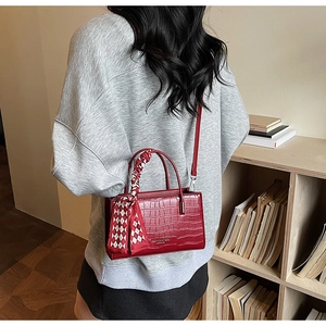 Detail of red croc-effect handbag with silk scarf and adjustable strap on a shoulder