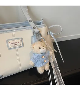 Detail of plush bear charm with blue knit cardigan on a leather shoulder bag